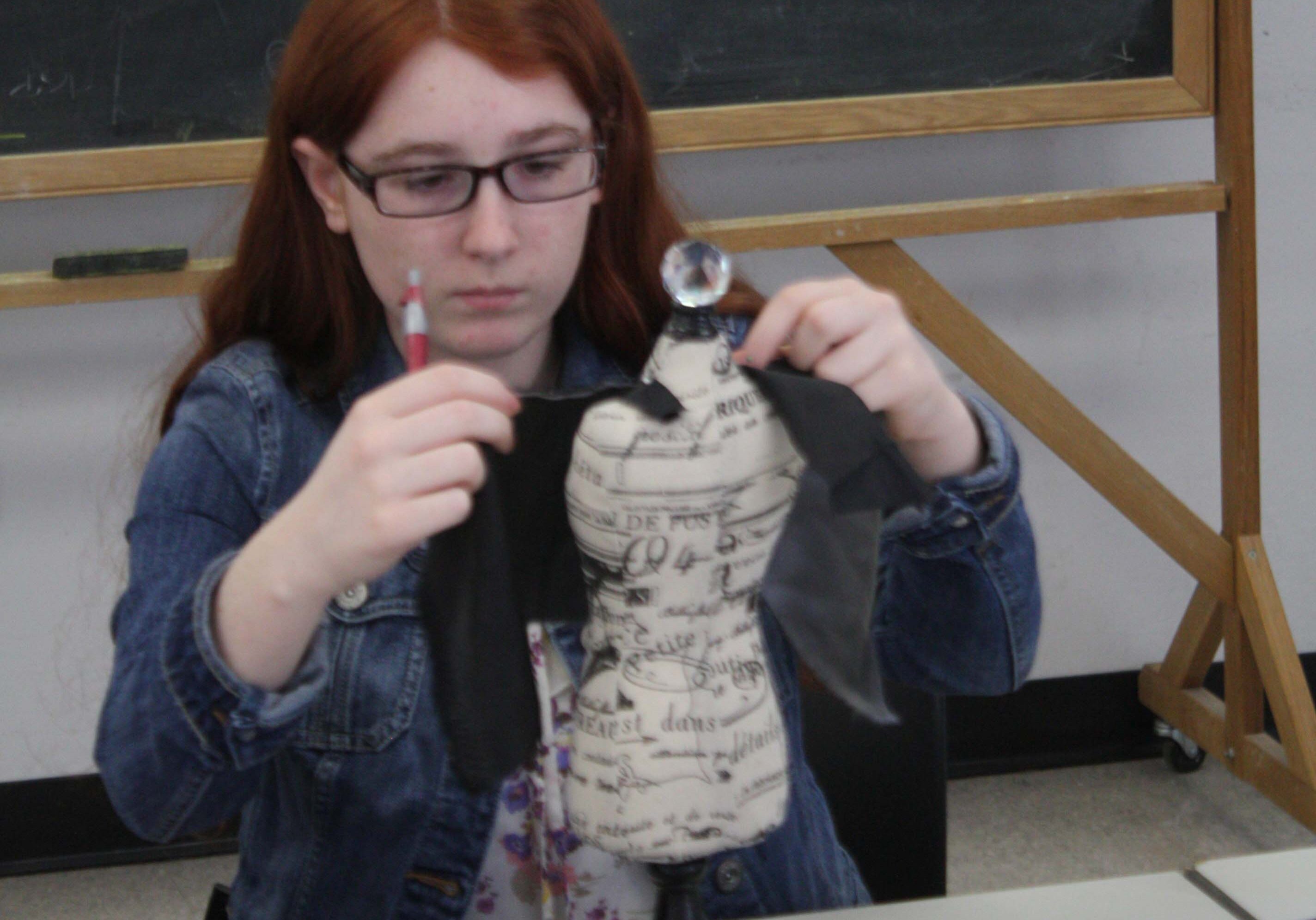 A participant in a teen program designs a dress on a miniature dress form A participant in a teen program designs a dress on a miniature dress form